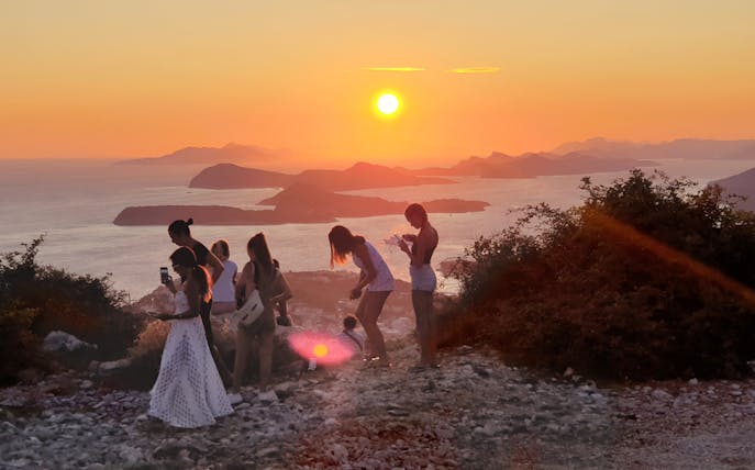 Group enjoying sunset view over Dubrovnik islands, raising a toast.