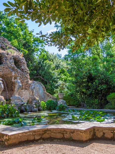 Stone grotto with statues and pond in lush garden, Game of Thrones driving tour location.