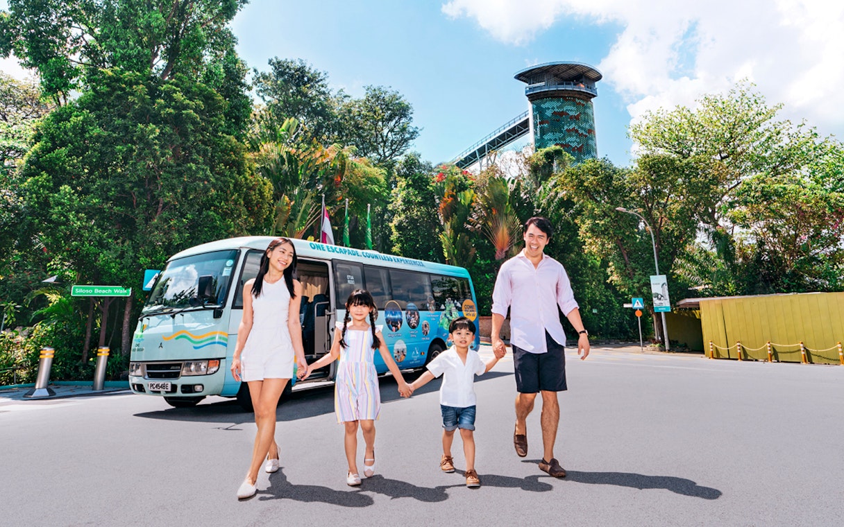 Family walking in front of a colorful tour bus on Sentosa Island.