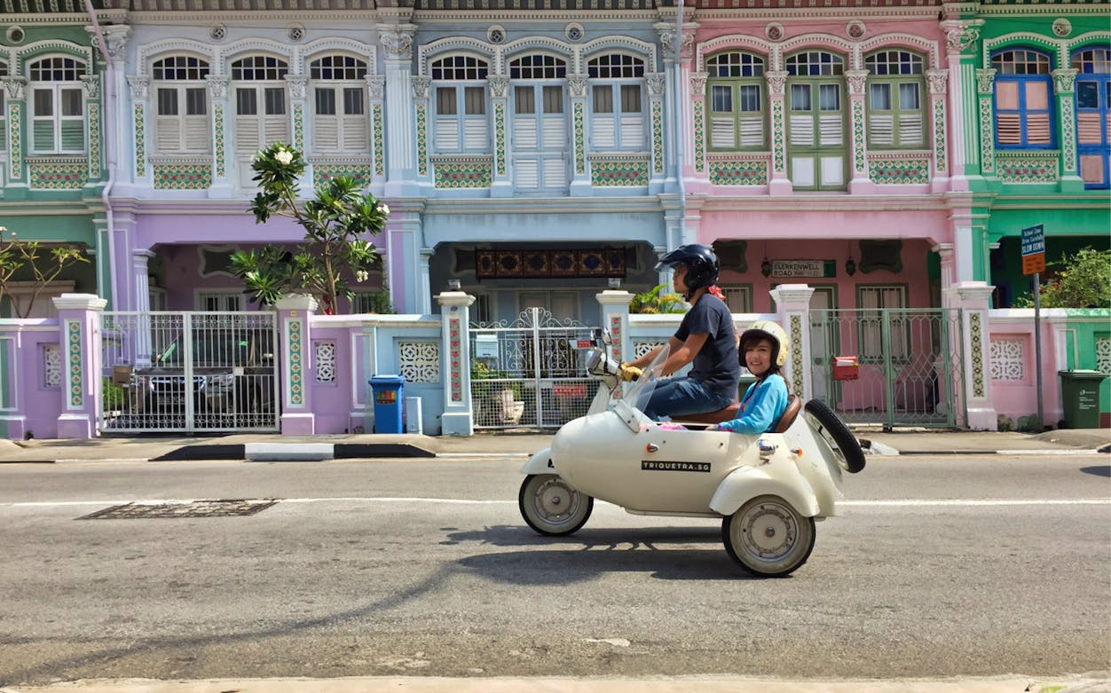 Sidecar tour passing colorful shophouses on Singapore street.