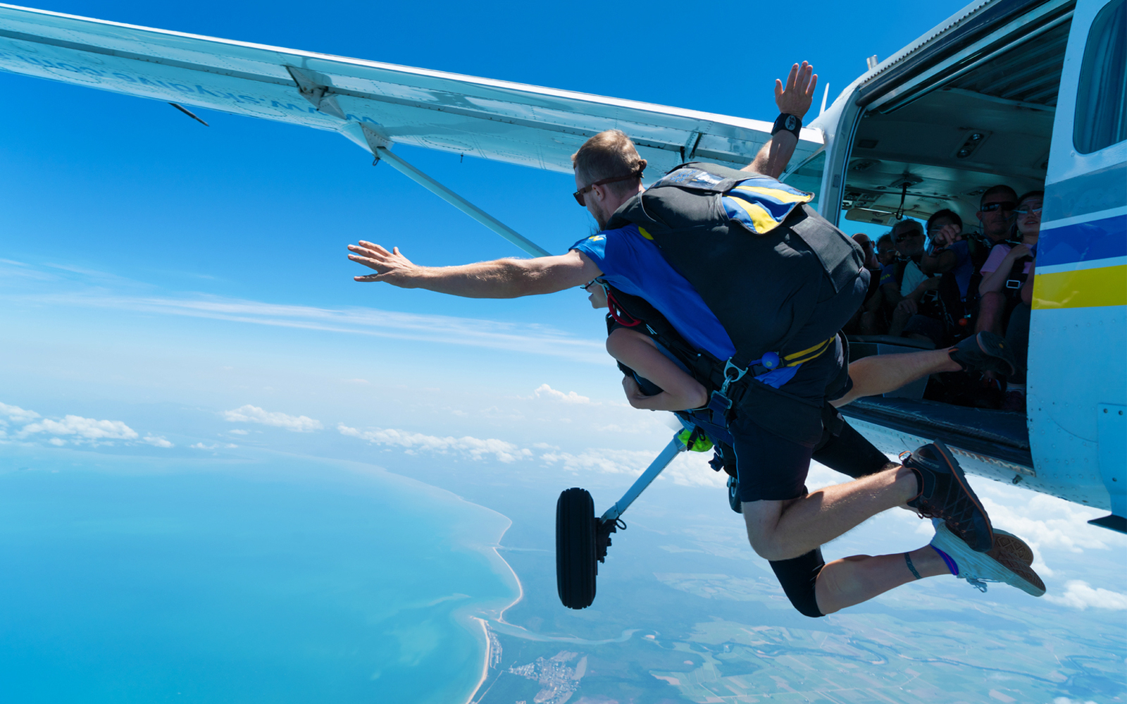 Skydivers jumping from plane over Mission Beach, Australia, during 15,000ft tandem skydive.