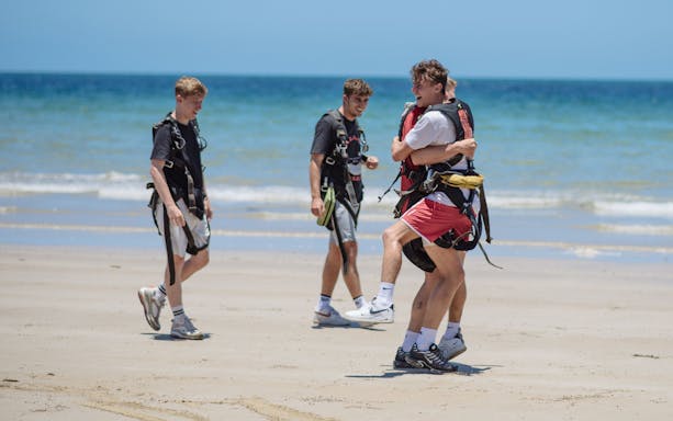 Skydivers celebrating on Mission Beach after 15,000ft tandem jump, ocean in background.