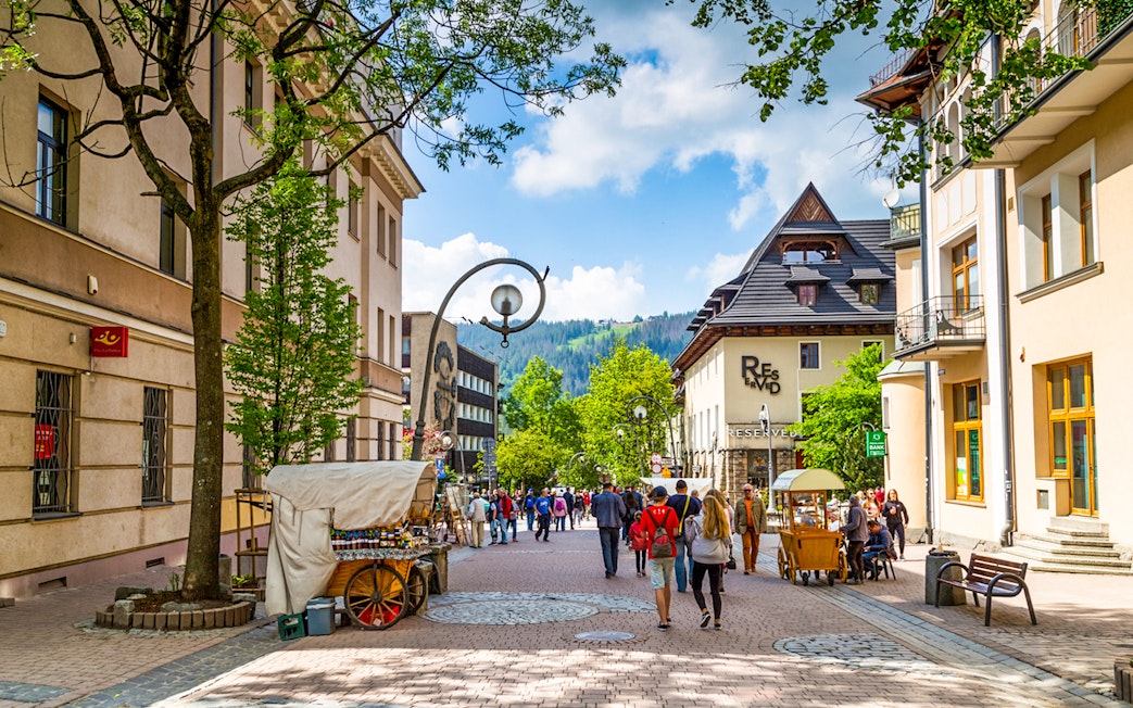 Krupówki Street in Zakopane with people walking and street vendors, Tatra Mountains in background.