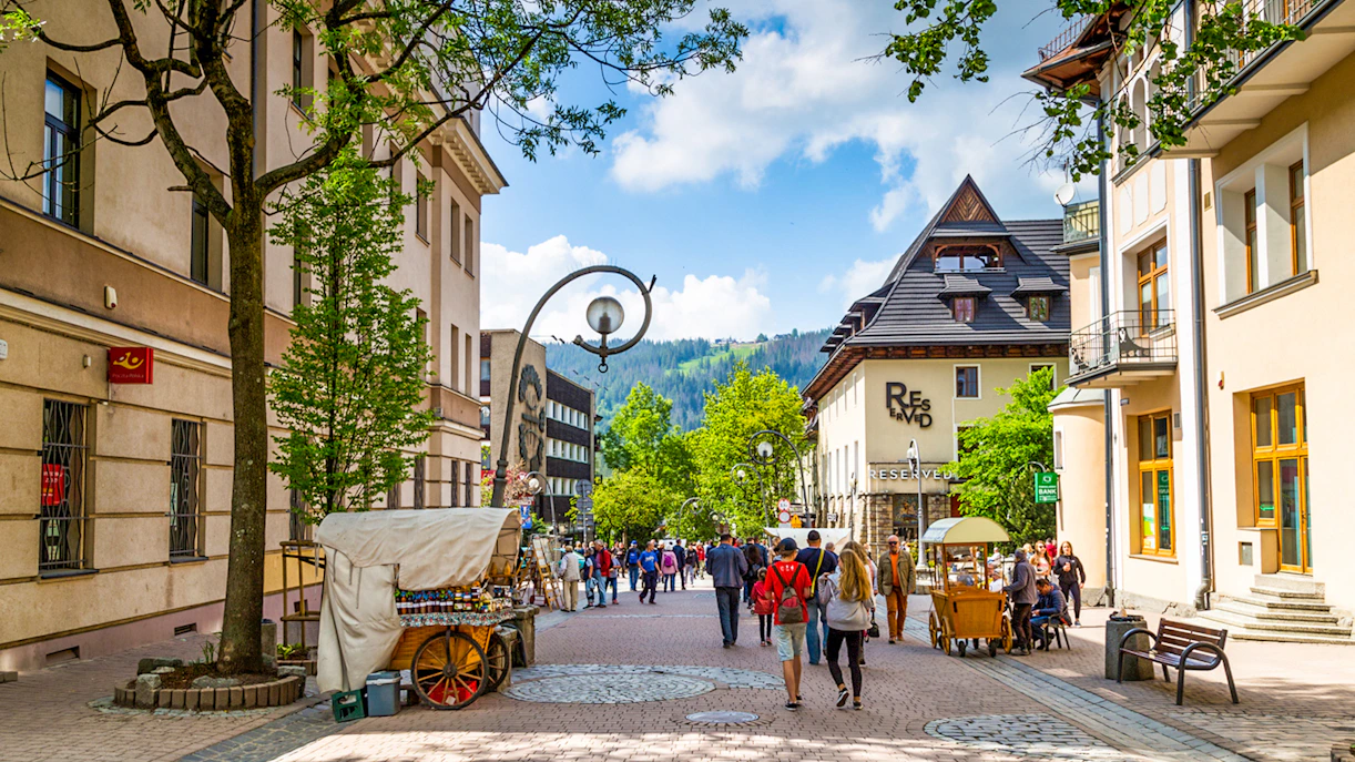 Krupówki Street in Zakopane with people walking and street vendors, Tatra Mountains in background.