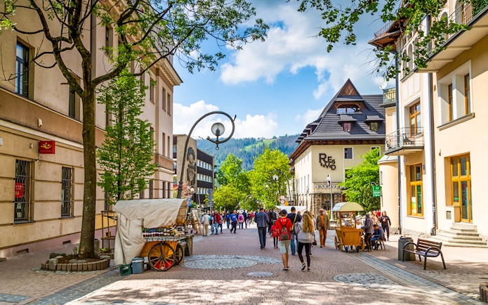 Krupówki Street in Zakopane with people walking and street vendors, Tatra Mountains in background.