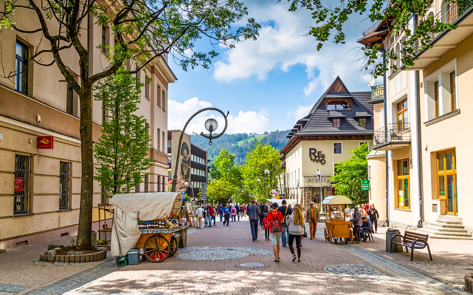 Krupówki Street in Zakopane with people walking and street vendors, Tatra Mountains in background.