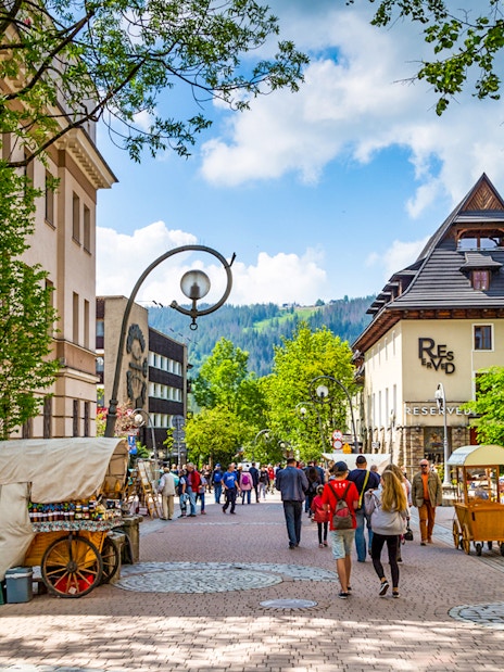 Krupówki Street in Zakopane with people walking and street vendors, Tatra Mountains in background.