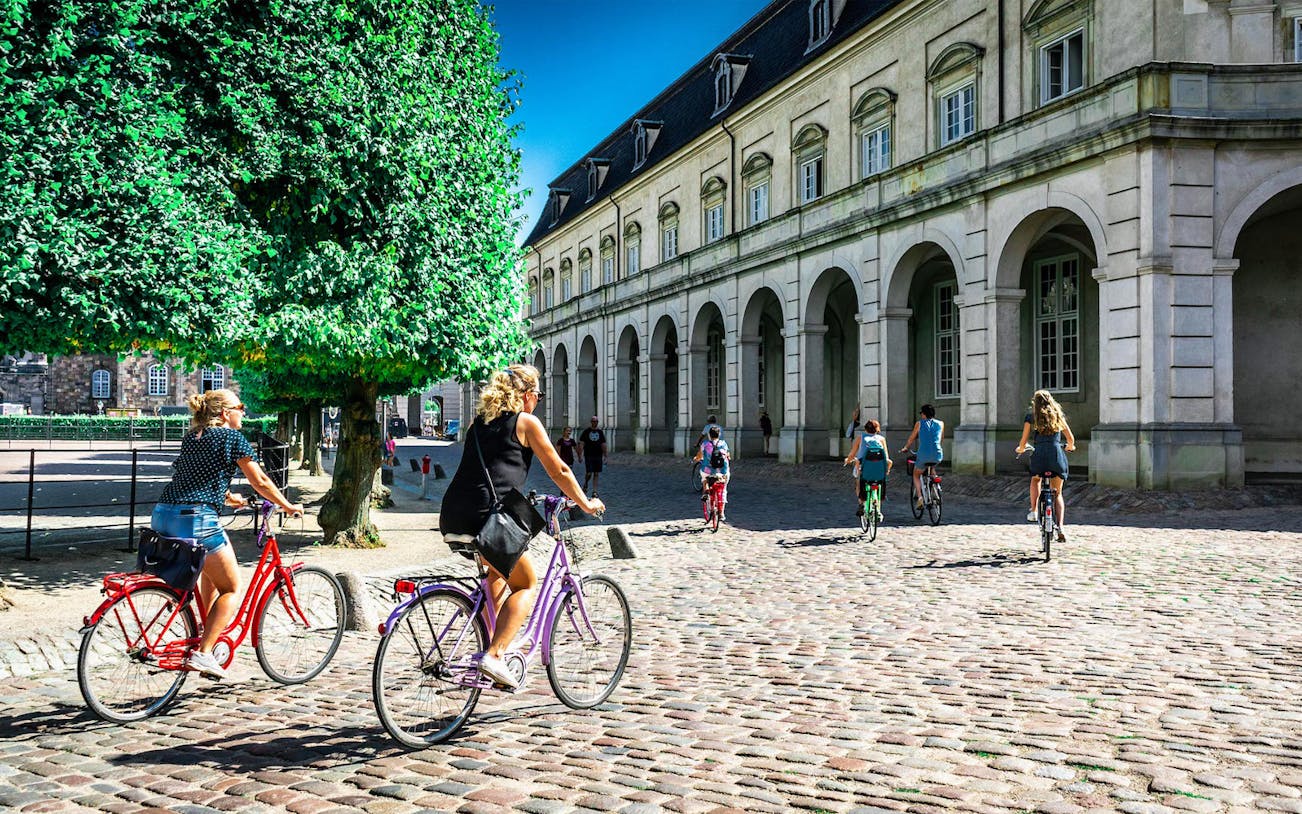 Cyclists riding past historic building on Copenhagen city bike tour.