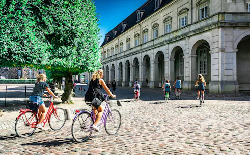 Cyclists riding past historic building on Copenhagen city bike tour.