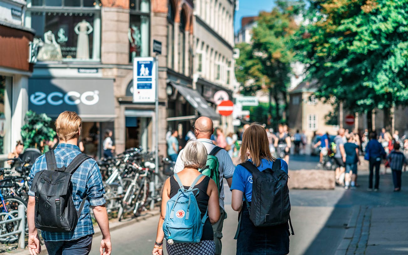 Tourists walking on a busy street in Copenhagen, Denmark, with shops and bicycles.