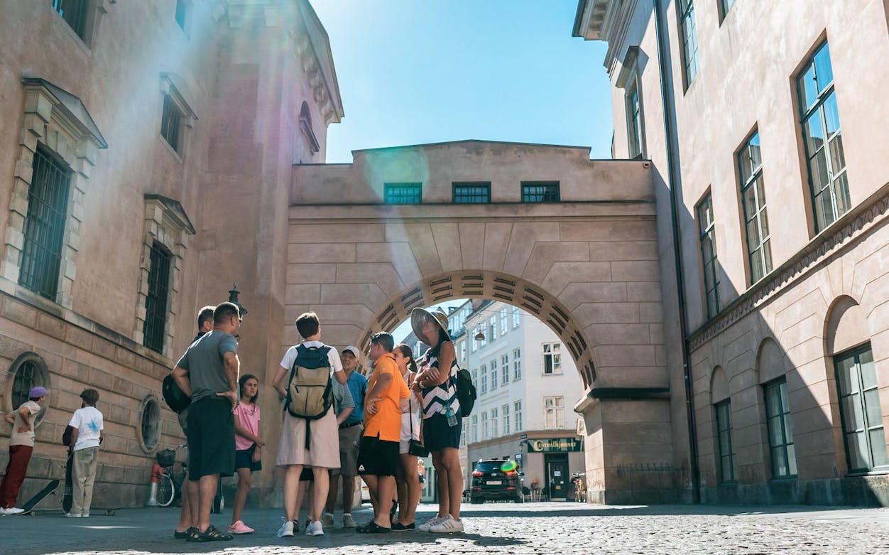 Group of tourists in Copenhagen Old Town under historic archway.