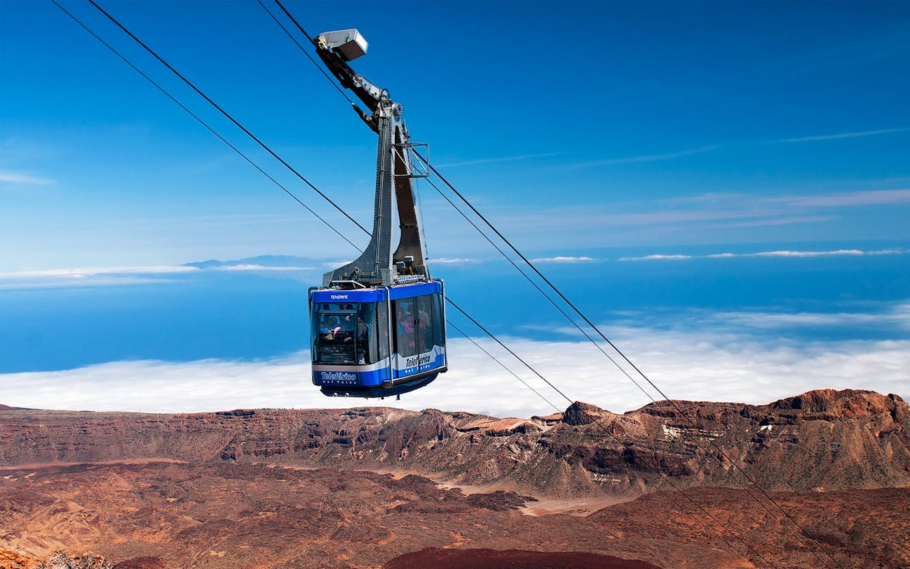 Cable car ascending Mount Teide with rocky landscape and clouds below.