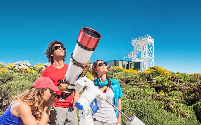 Visitors using a telescope at Teide Observatory, Tenerife, with surrounding landscape.