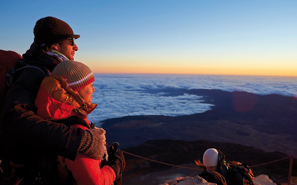 Couple enjoying sunset view from Mount Teide with clouds below.