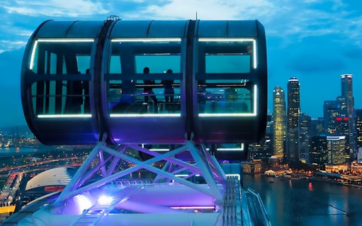Singapore Flyer capsule overlooking Marina Bay Sands and city skyline at dusk.