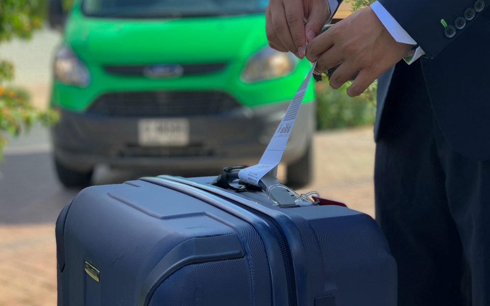 Luggage being tagged for DUBZ home check-in service with a green van in the background.