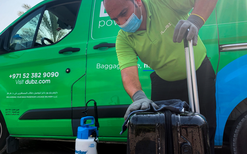 DUBZ staff sanitizing luggage beside a branded van for home check-in service.