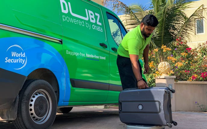 Man handling luggage beside DUBZ home check-in service van.