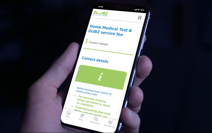 Hand holding smartphone displaying DUBZ Home PCR Test booking page.