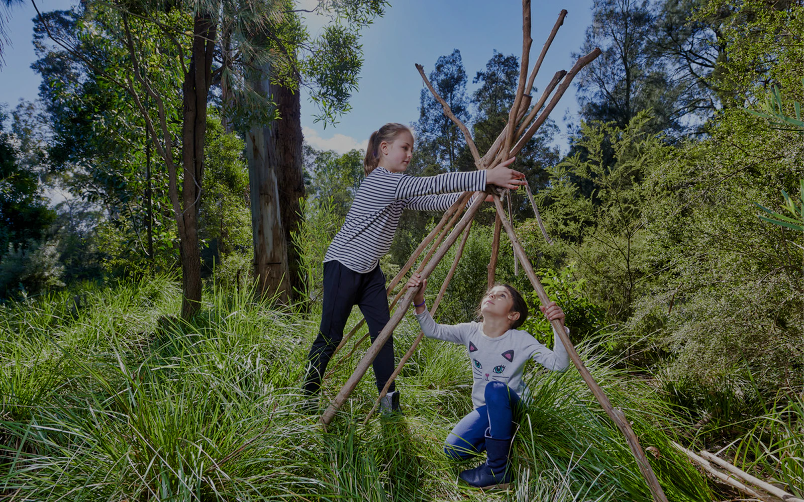 Children building a stick shelter at Healesville Sanctuary, surrounded by lush greenery.