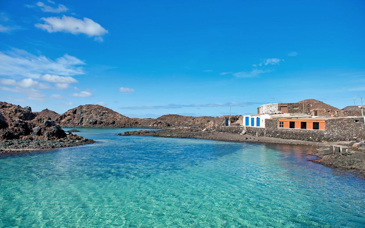 Lobos Island coastline with clear blue water and rustic buildings.