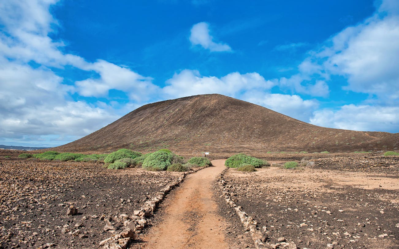 Pathway leading to a volcanic hill on Lobos Island under a blue sky.