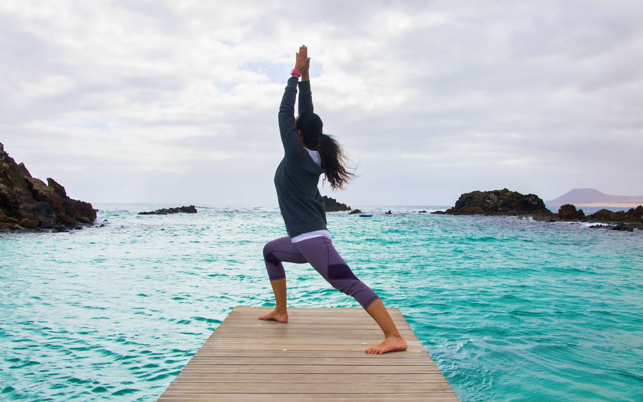 Person practicing yoga on a dock at Lobos Island with ocean view.
