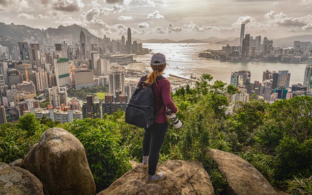 Hiker overlooking Hong Kong skyline from Victoria Peak during evening tour.
