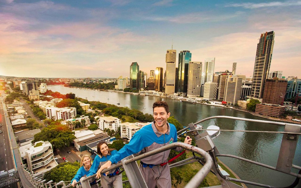 Climbers ascending Brisbane's Story Bridge with city skyline and river view.