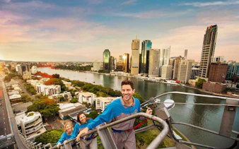 Climbers ascending Brisbane's Story Bridge with city skyline and river view.