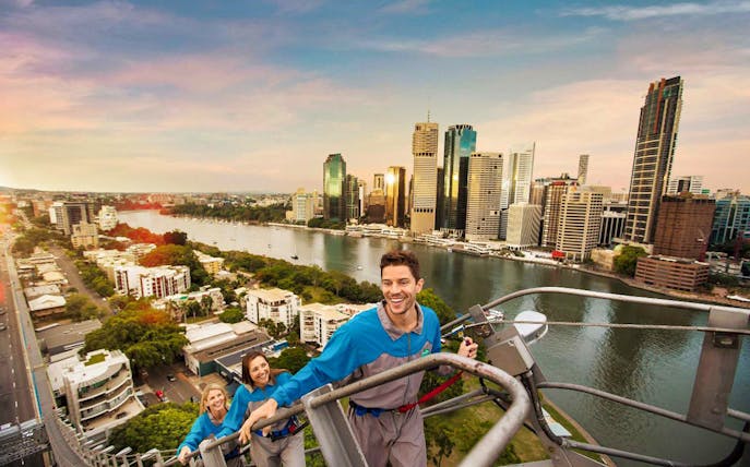 Climbers ascending Brisbane's Story Bridge with city skyline and river view.