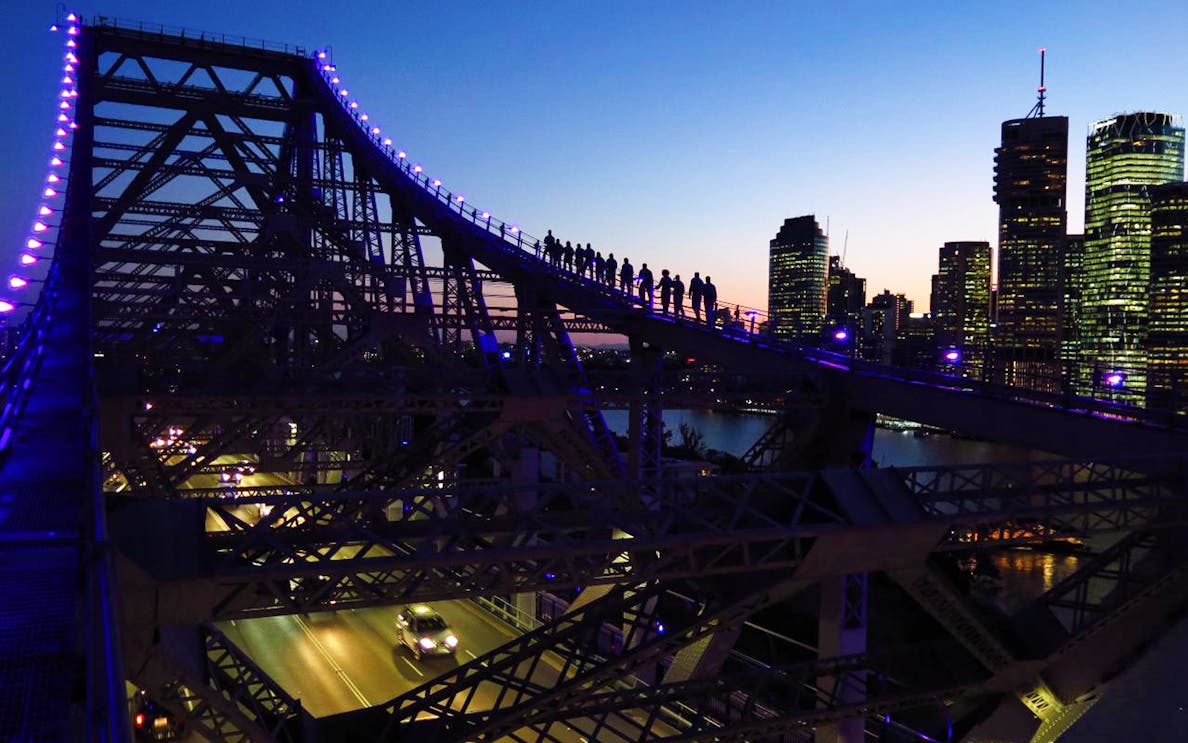 Climbers on Brisbane Story Bridge at dusk with city skyline in background.