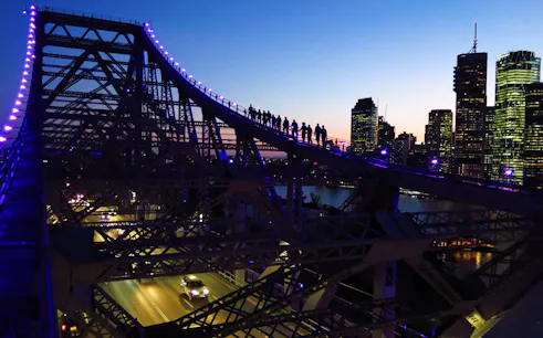 Climbers on Brisbane Story Bridge at dusk with city skyline in background.