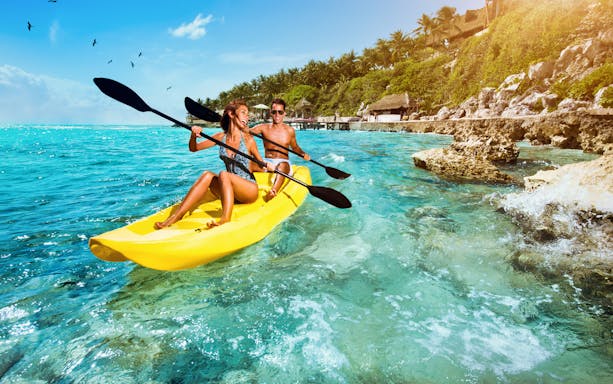Couple kayaking in clear waters near rocky shore, Isla Mujeres.