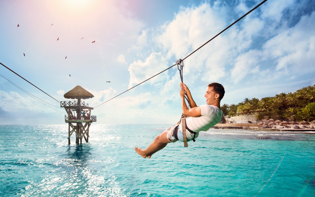 Person ziplining over turquoise water at Garrafón Reef Natural Park, Isla Mujeres.