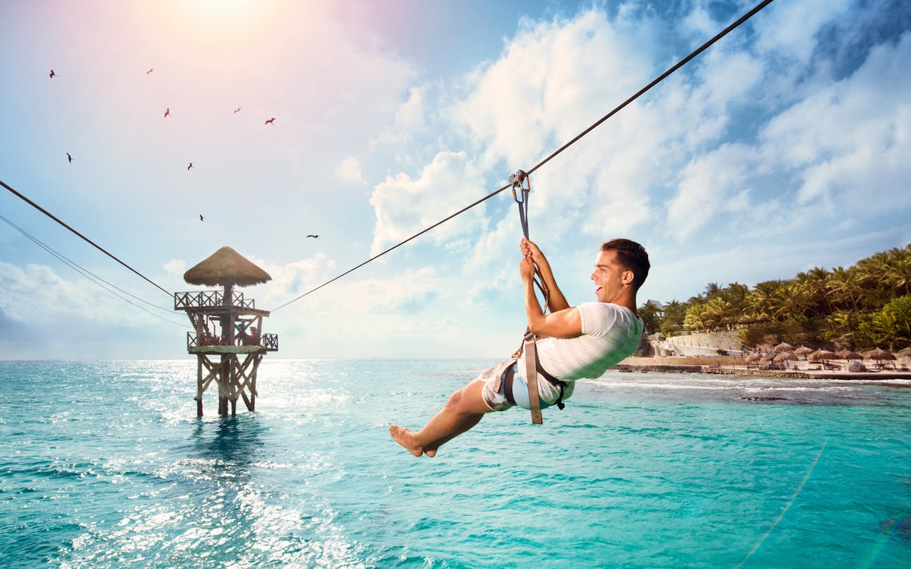 Person ziplining over turquoise water at Garrafón Reef Natural Park, Isla Mujeres.