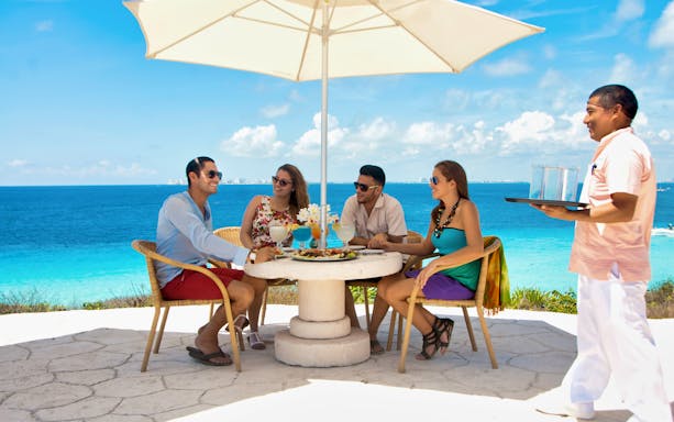 Group dining under umbrella with ocean view at Garrafón Reef Natural Park, Isla Mujeres.