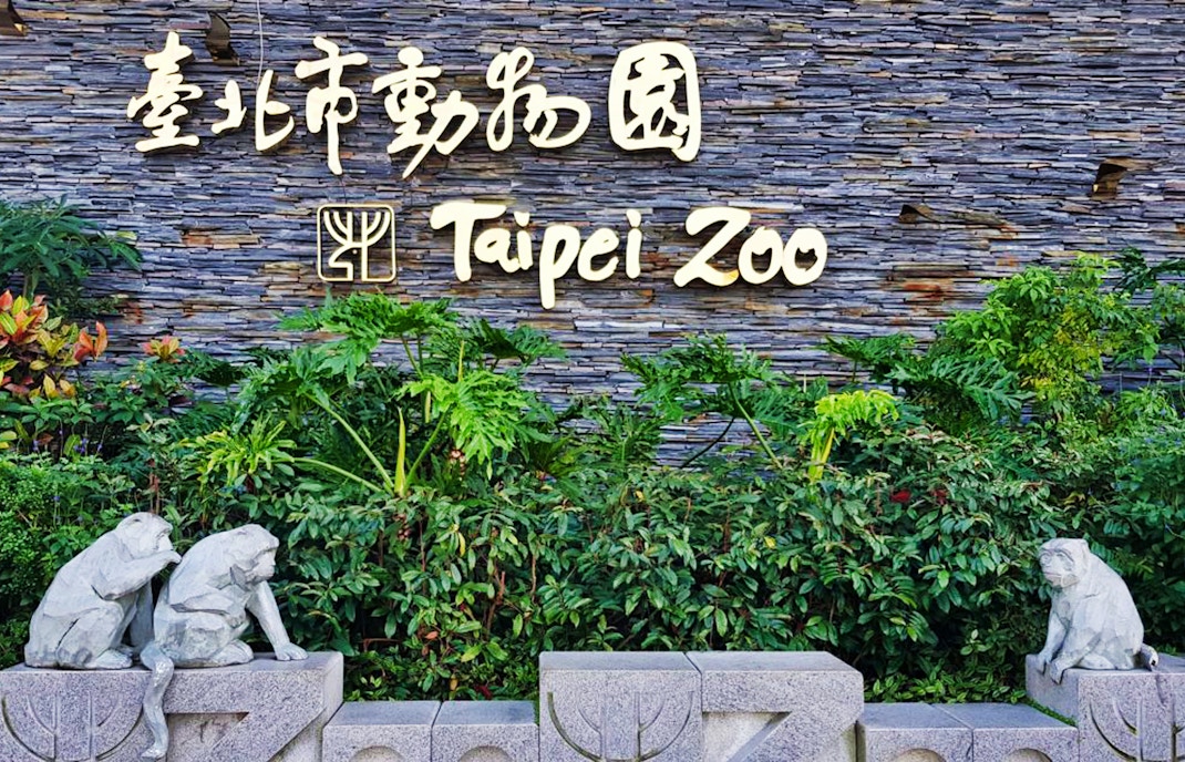Taipei Zoo entrance sign with stone monkey sculptures and greenery.