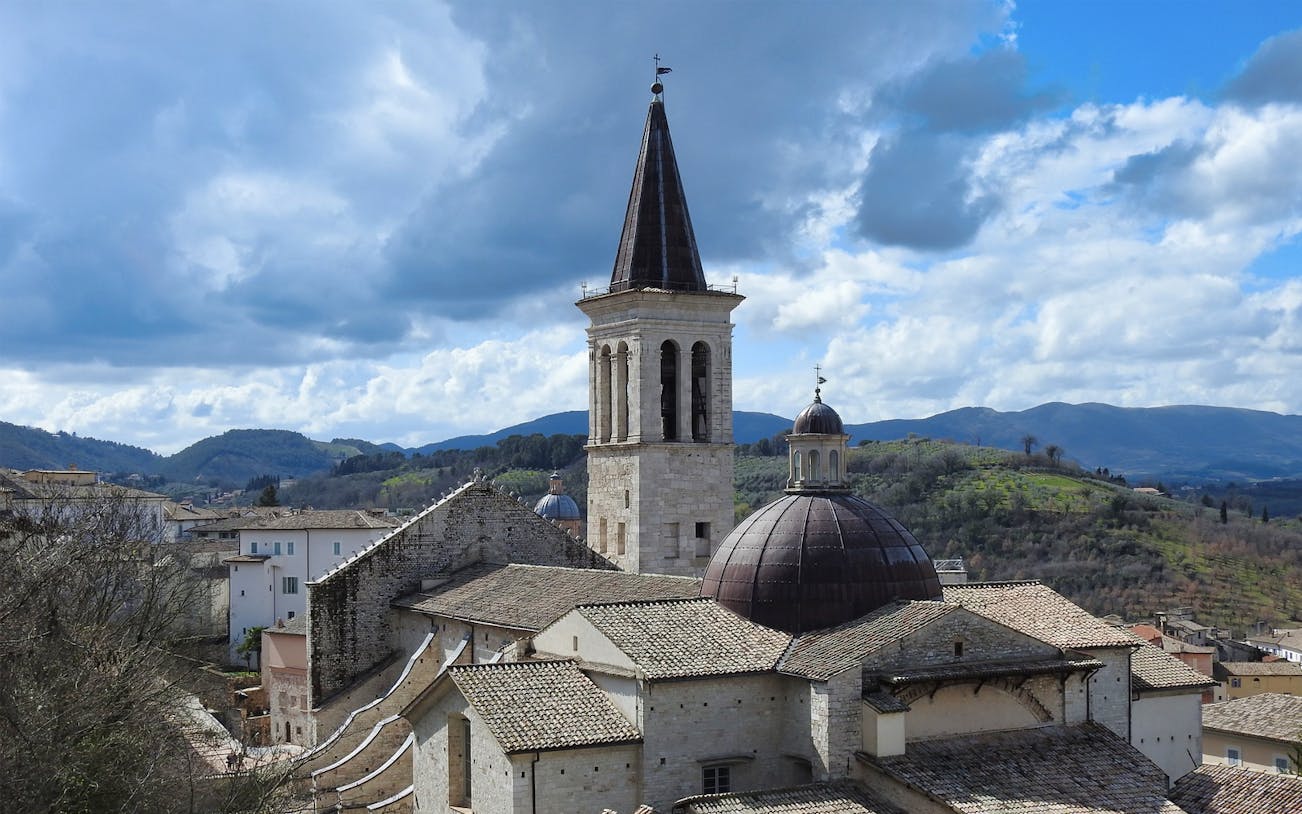 Duomo di Spoleto with bell tower and dome against a hilly landscape.