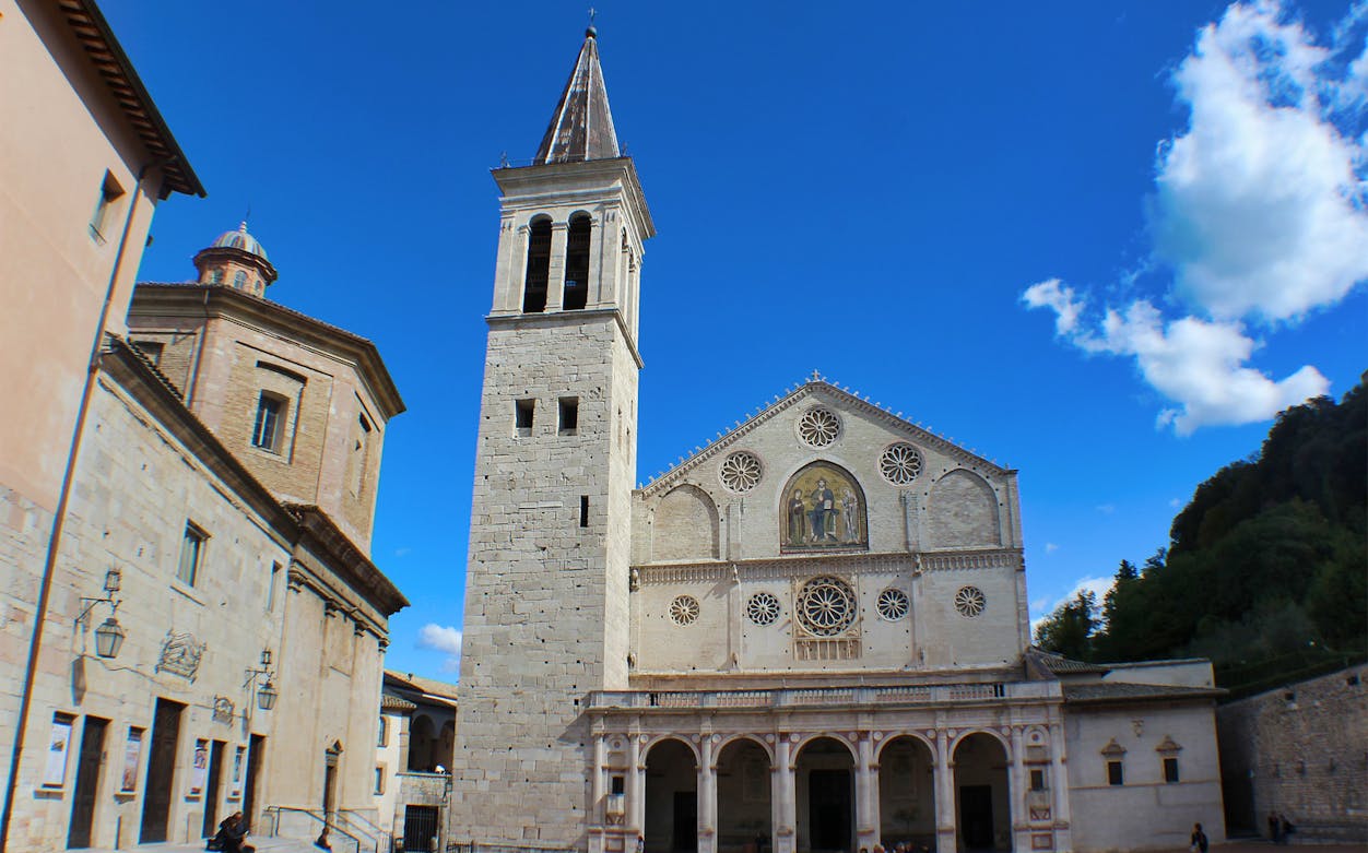 Duomo di Spoleto facade with bell tower under blue sky.