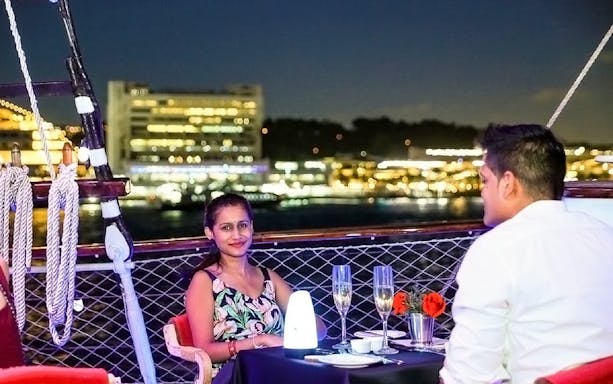Couple dining on The Royal Albatross sail with city lights in the background.