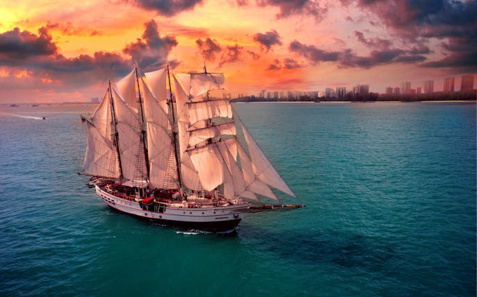 Sailing ship Royal Albatross at sunset near city skyline.