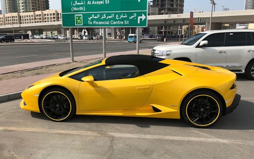 Yellow luxury supercar parked on a city street near Al Asayel St sign in Dubai.