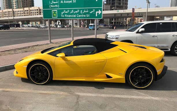 Yellow luxury supercar parked on a city street near Al Asayel St sign in Dubai.