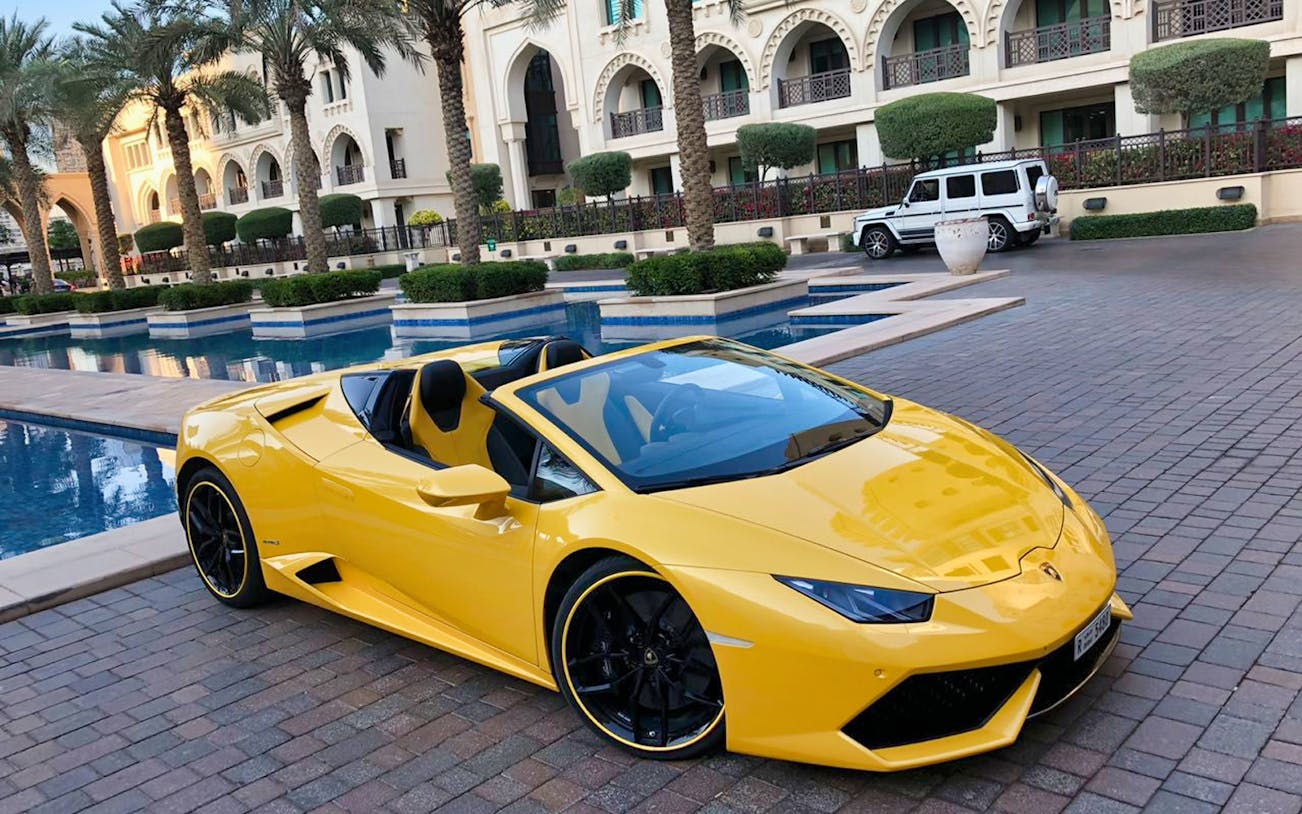 Yellow luxury supercar parked by a poolside at a resort.