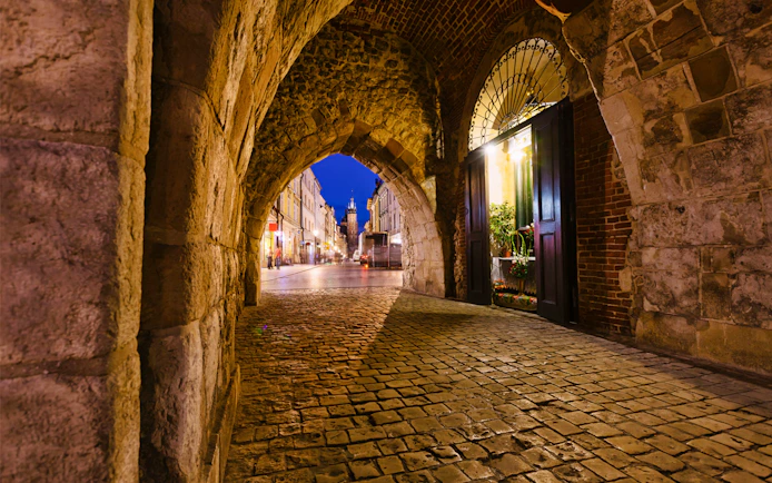 Krakow city street view through a stone archway at night.