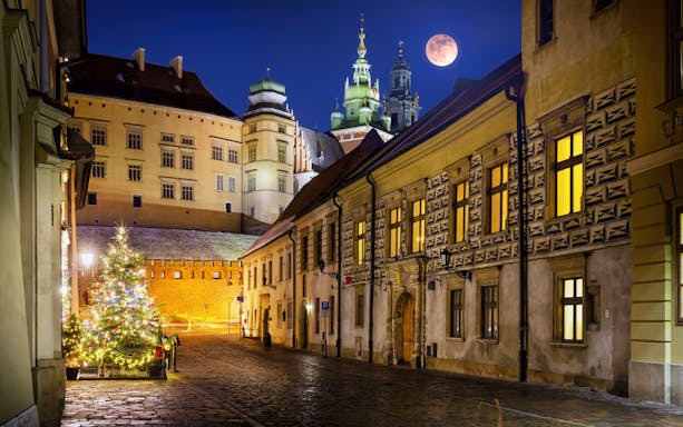 Krakow street at night with illuminated buildings and a full moon.