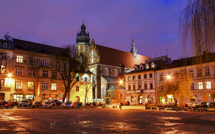 Krakow city square at dusk with illuminated historic buildings and church tower.