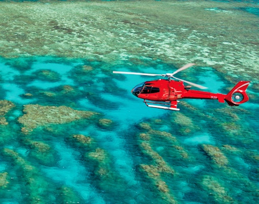 Red helicopter flying over the Great Barrier Reef's turquoise waters.