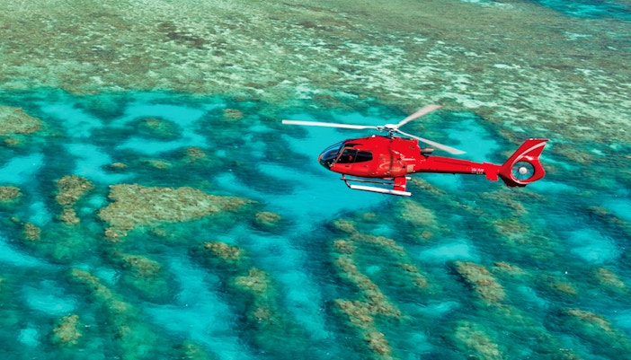 Red helicopter flying over the Great Barrier Reef's turquoise waters.